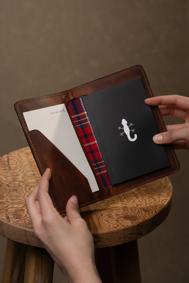 Hands holding an open leather notebook cover with a notebook inside