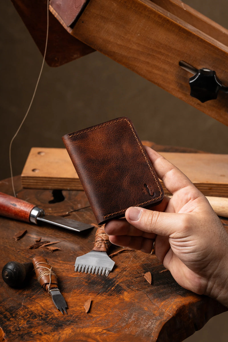 Hand holding a full grain leather bifold wallet at a workbench