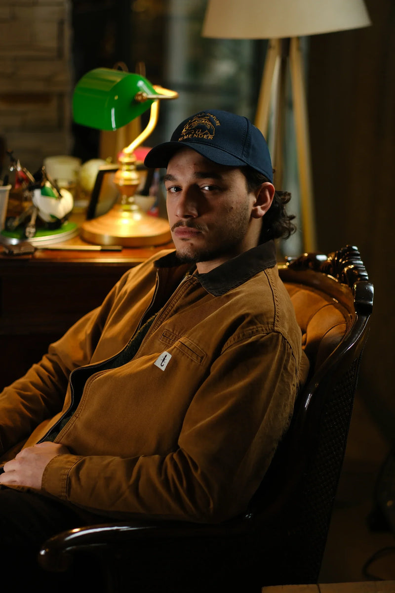 Man wearing a tan canvas jacket and a navy cap