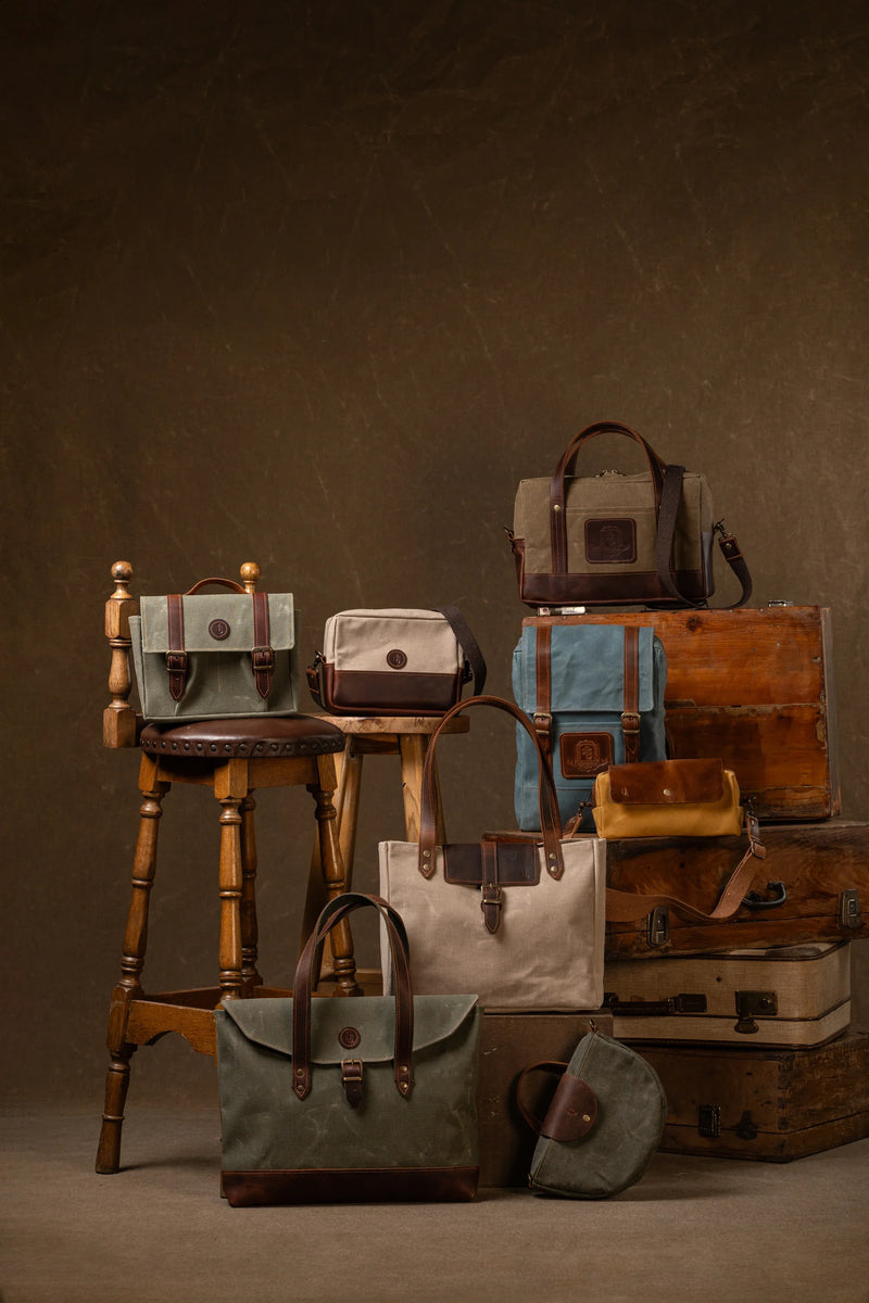 Waxed canvas and leather bags arranged on vintage trunks and stools