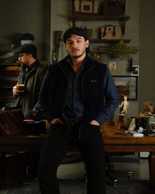 Man in a dark coat standing in a room with wooden furniture and decor.